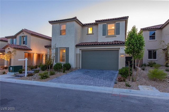 mediterranean / spanish-style house with an attached garage, stucco siding, a tile roof, and decorative driveway