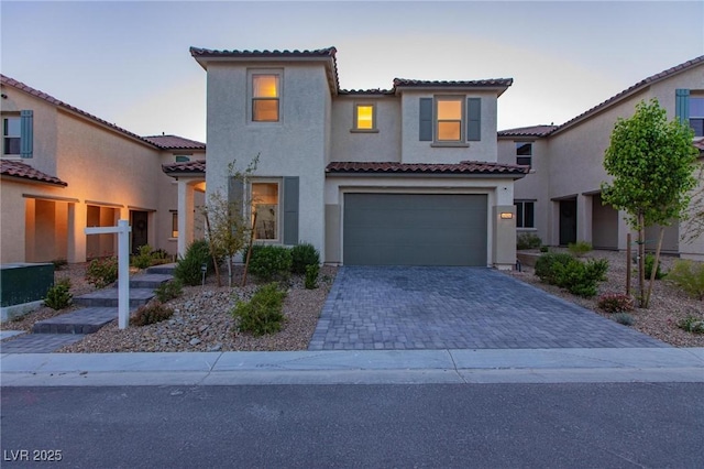 mediterranean / spanish home with a tile roof, a garage, driveway, and stucco siding