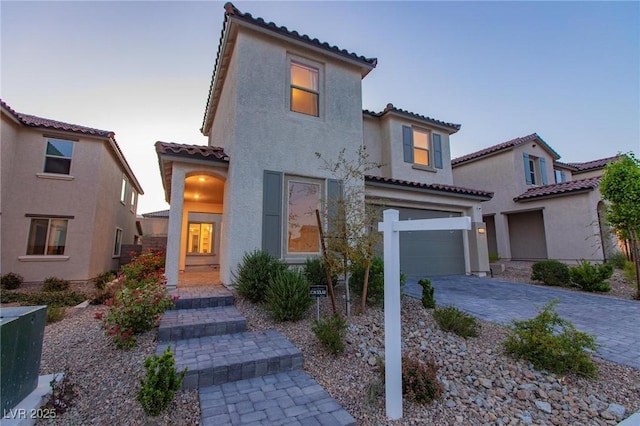 mediterranean / spanish house with an attached garage, a tiled roof, stucco siding, and decorative driveway