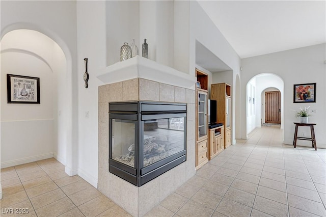 unfurnished living room with arched walkways, light tile patterned flooring, a tiled fireplace, and baseboards