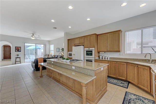 kitchen with white appliances, light tile patterned floors, visible vents, arched walkways, and a sink
