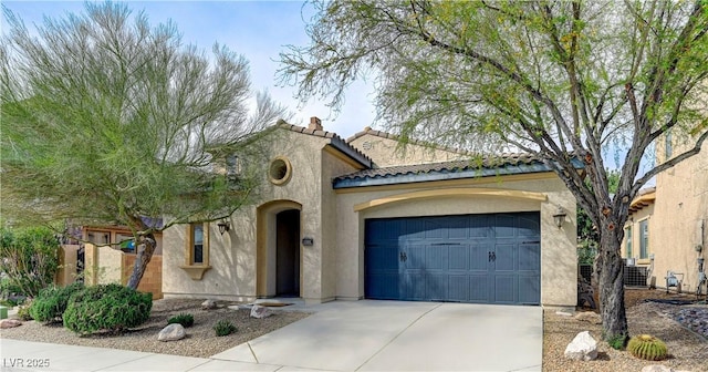 mediterranean / spanish home featuring an attached garage, a tiled roof, driveway, and stucco siding