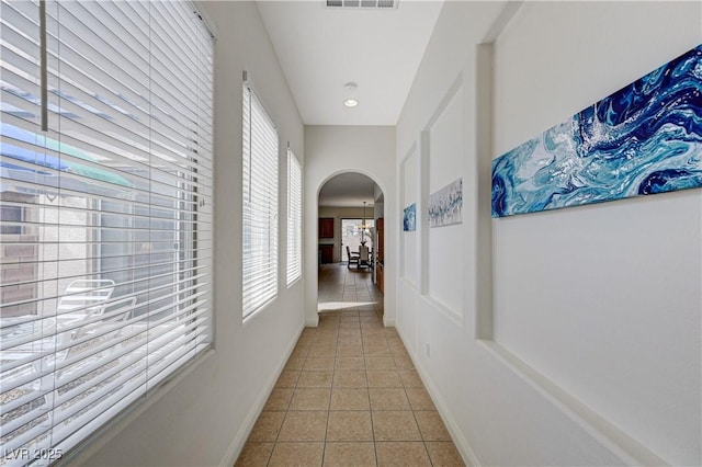 hall featuring visible vents, tile patterned floors, arched walkways, and baseboards