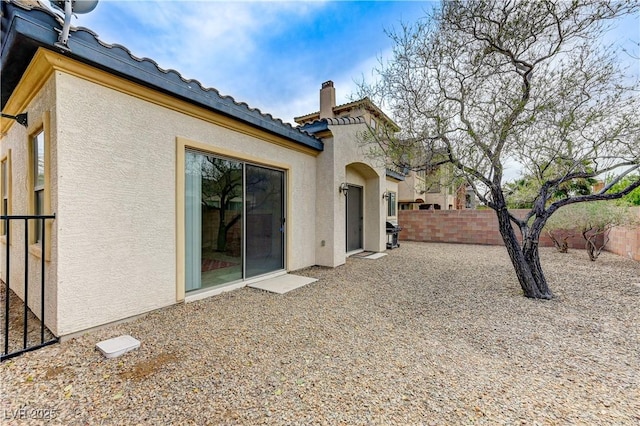 rear view of house with a chimney, a tile roof, fence, and stucco siding