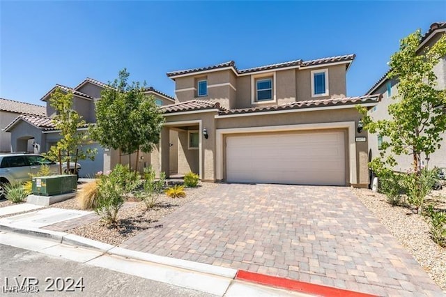 mediterranean / spanish house featuring stucco siding, a tile roof, an attached garage, and decorative driveway