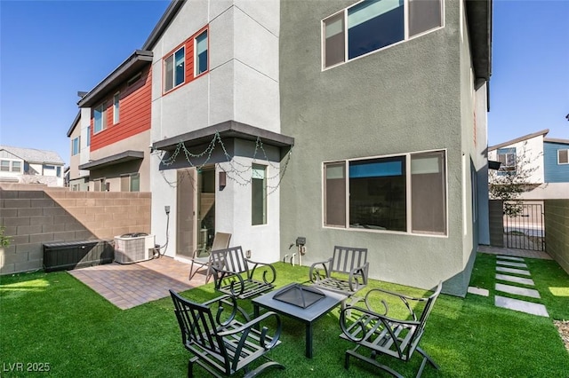 rear view of property with a lawn, a patio area, central AC, fence, and stucco siding