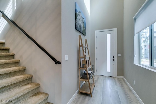 foyer featuring baseboards, a high ceiling, light wood-type flooring, and stairs