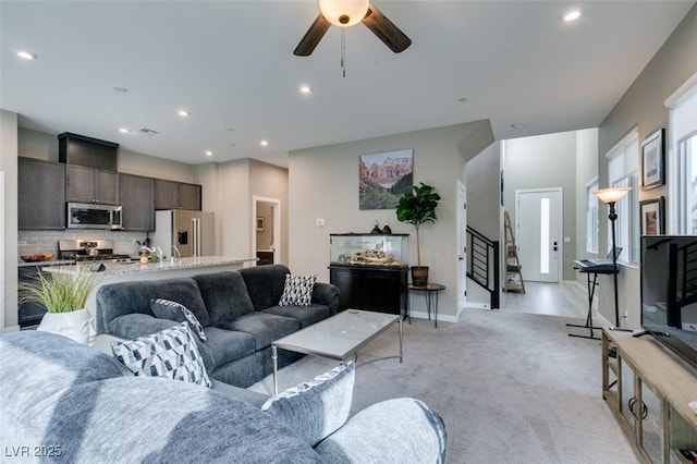 living area featuring stairs, baseboards, ceiling fan, light colored carpet, and recessed lighting
