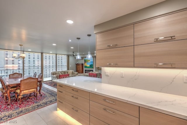 kitchen with light stone counters, light brown cabinets, light tile patterned floors, a chandelier, and open floor plan