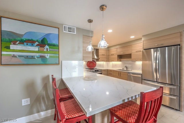 kitchen featuring light stone counters, wall chimney range hood, visible vents, a peninsula, and appliances with stainless steel finishes