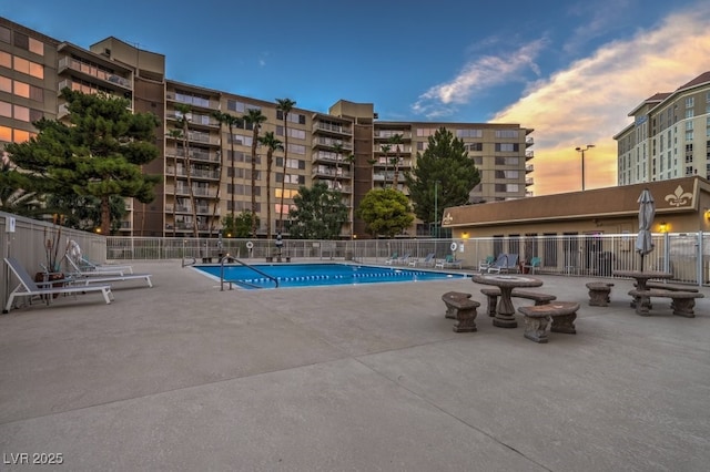 pool at dusk with a community pool, fence, and a patio