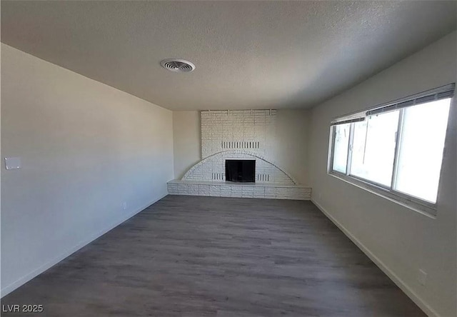 3749 Ponderosa Ave, Las Vegas, NV 89115 - unfurnished living room featuring a textured ceiling, visible vents, a brick fireplace, and dark wood finished floors