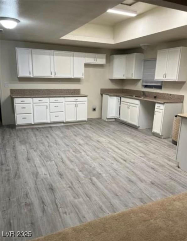 664 Sky Rd, Indian Springs, NV 89018 - kitchen with white cabinets, light wood-style flooring, dark countertops, and a raised ceiling