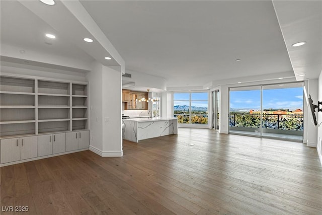 unfurnished living room with baseboards, a sink, recessed lighting, and wood-type flooring