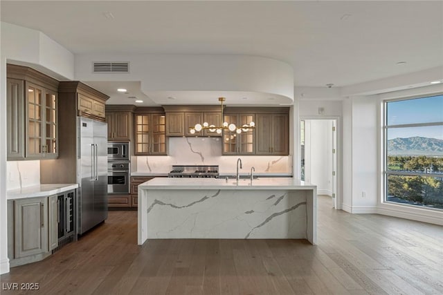 kitchen with a sink, a center island with sink, visible vents, a chandelier, and built in appliances