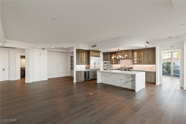 kitchen with a sink, a notable chandelier, built in appliances, light countertops, and dark wood-type flooring