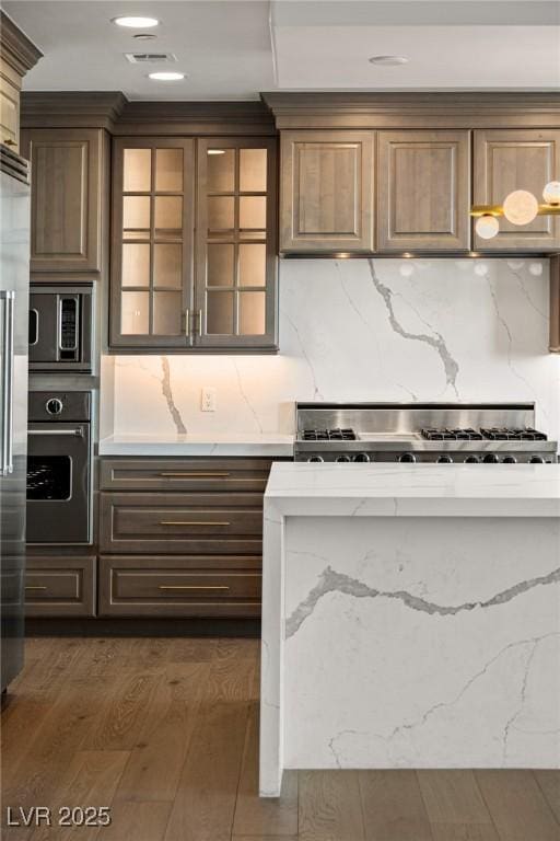 kitchen featuring tasteful backsplash, glass insert cabinets, stainless steel appliances, dark wood-style flooring, and light stone countertops