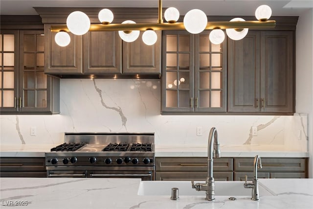 kitchen featuring dark brown cabinetry, glass insert cabinets, decorative backsplash, light stone counters, and range with two ovens
