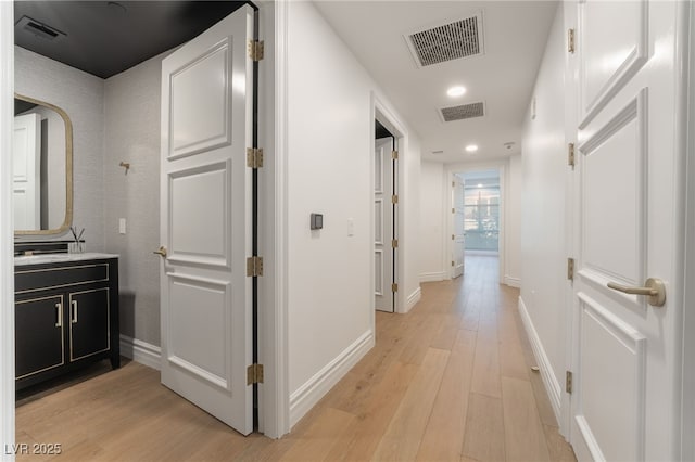 corridor featuring baseboards, visible vents, and light wood-style flooring