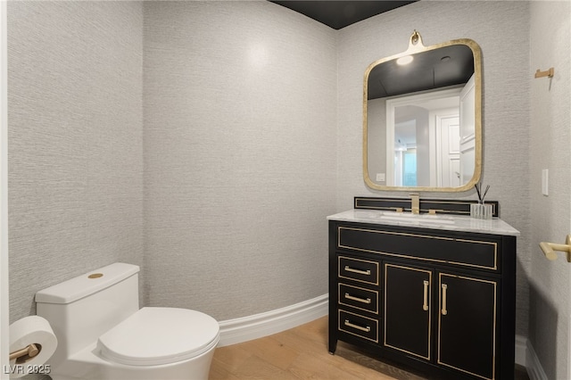 half bathroom with baseboards, wood finished floors, toilet, and vanity