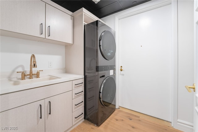 laundry room featuring stacked washer / drying machine, light wood-style floors, cabinet space, and a sink