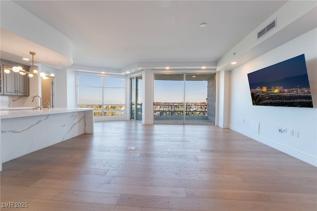 unfurnished living room with light wood-style floors, visible vents, baseboards, and a notable chandelier