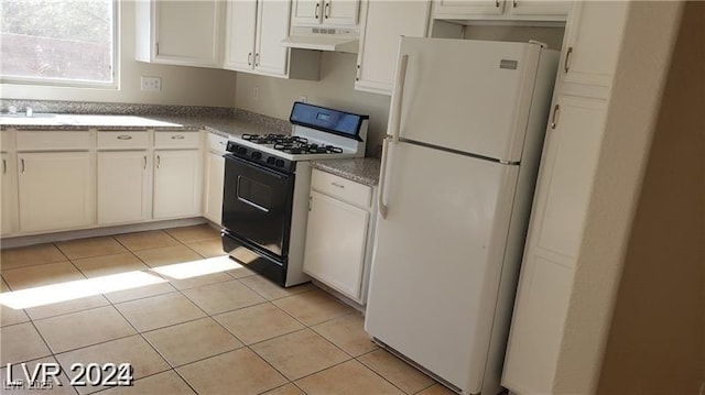 kitchen featuring light tile patterned flooring, range with gas stovetop, under cabinet range hood, white cabinetry, and freestanding refrigerator