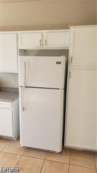 kitchen with freestanding refrigerator, white cabinets, and light tile patterned flooring