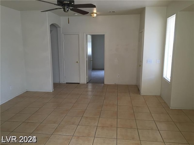 unfurnished room with arched walkways, ceiling fan, and light tile patterned floors