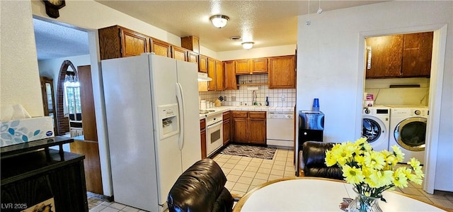kitchen featuring white appliances, tasteful backsplash, under cabinet range hood, a sink, and washer and dryer