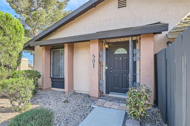 view of exterior entry with stucco siding and fence