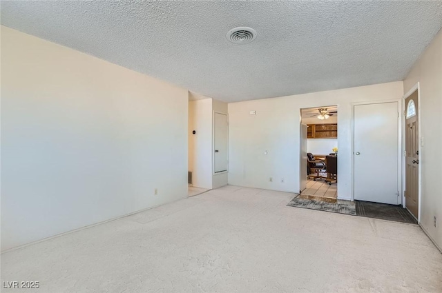 empty room featuring carpet, visible vents, a textured ceiling, and a ceiling fan
