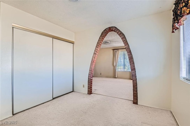 unfurnished bedroom with a closet, arched walkways, a textured ceiling, and carpet floors