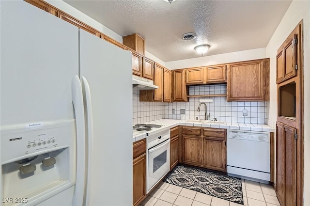 kitchen with visible vents, a sink, white appliances, under cabinet range hood, and brown cabinetry