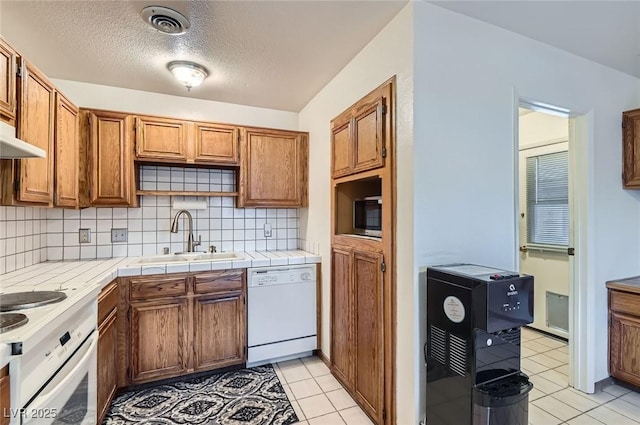 kitchen featuring a sink, light tile patterned floors, decorative backsplash, and white appliances