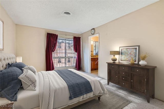 bedroom with a textured ceiling, light colored carpet, visible vents, and connected bathroom