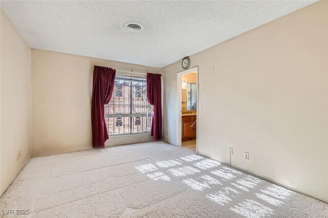 spare room featuring visible vents, light colored carpet, and a textured ceiling