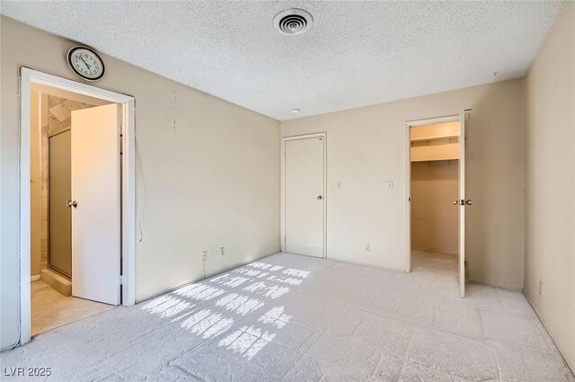 unfurnished bedroom featuring a textured ceiling, light colored carpet, a spacious closet, and visible vents