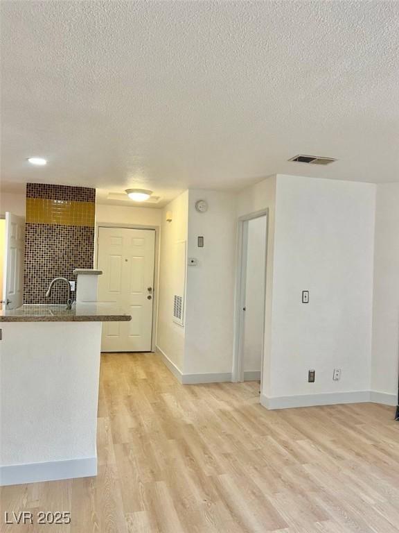 interior space featuring baseboards, light wood-type flooring, a textured ceiling, and visible vents