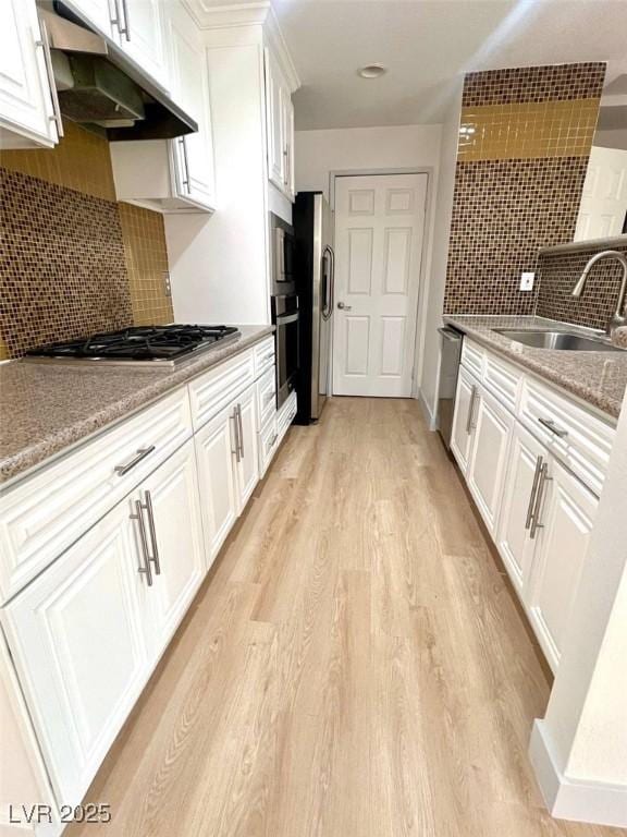 kitchen with white cabinets, appliances with stainless steel finishes, a sink, light wood finished floors, and under cabinet range hood