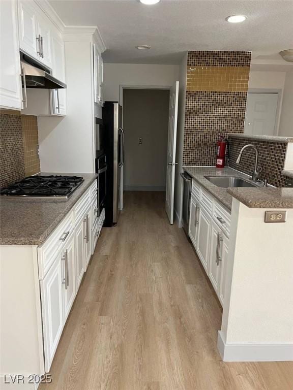 kitchen featuring white cabinets, a sink, light wood-style floors, tasteful backsplash, and under cabinet range hood