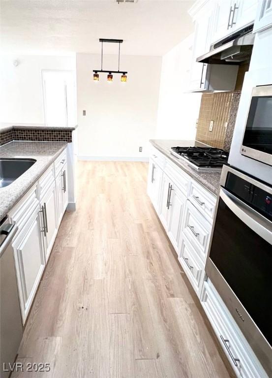 kitchen with appliances with stainless steel finishes, tasteful backsplash, light stone countertops, under cabinet range hood, and light wood-style flooring