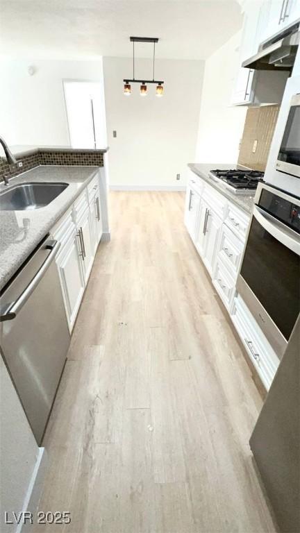kitchen featuring appliances with stainless steel finishes, a sink, light wood-style floors, under cabinet range hood, and white cabinetry