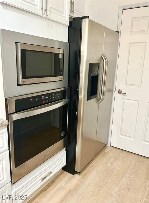 kitchen featuring light wood-style floors, appliances with stainless steel finishes, white cabinets, and light stone countertops