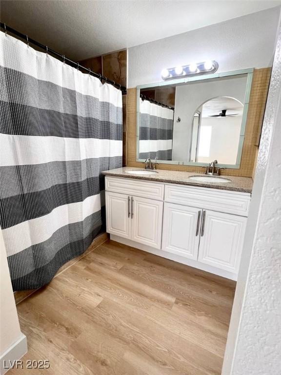full bath with a sink, a shower with curtain, double vanity, and wood finished floors