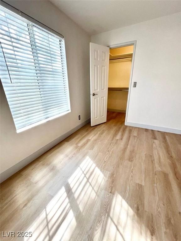 unfurnished bedroom featuring baseboards, light wood-type flooring, and a spacious closet