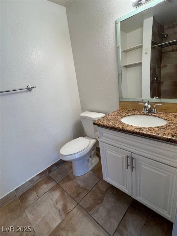 bathroom with vanity, a textured wall, a tile shower, and toilet