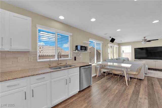 kitchen with stainless steel appliances, decorative backsplash, a sink, white cabinets, and wood finished floors