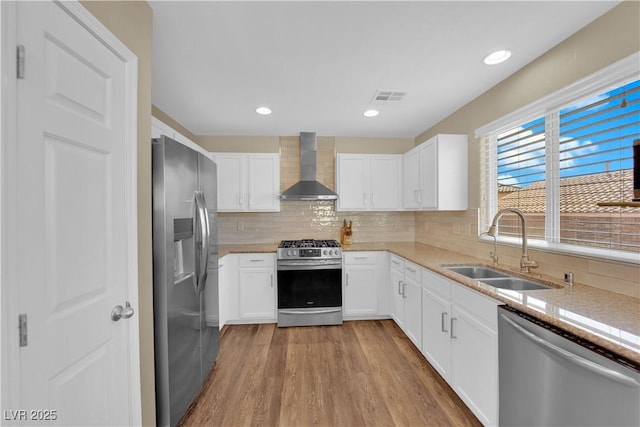 kitchen with visible vents, wood finished floors, stainless steel appliances, a sink, and wall chimney range hood
