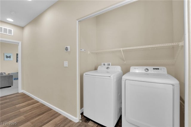 clothes washing area featuring washing machine and dryer, visible vents, wood finished floors, and laundry area